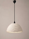 A modern pendant light with a textured, dome-shaped off-white shade and a matte black suspension rod and canopy, shown against a solid warm beige background.