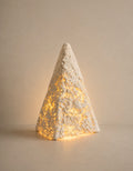 A textured white cone-shaped decorative lamp with warm yellow fairy lights glowing through its open weave, set against a neutral beige background.