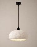 A textured white wide-dome pendant light with a matte black cord and canopy, shown against a soft neutral background