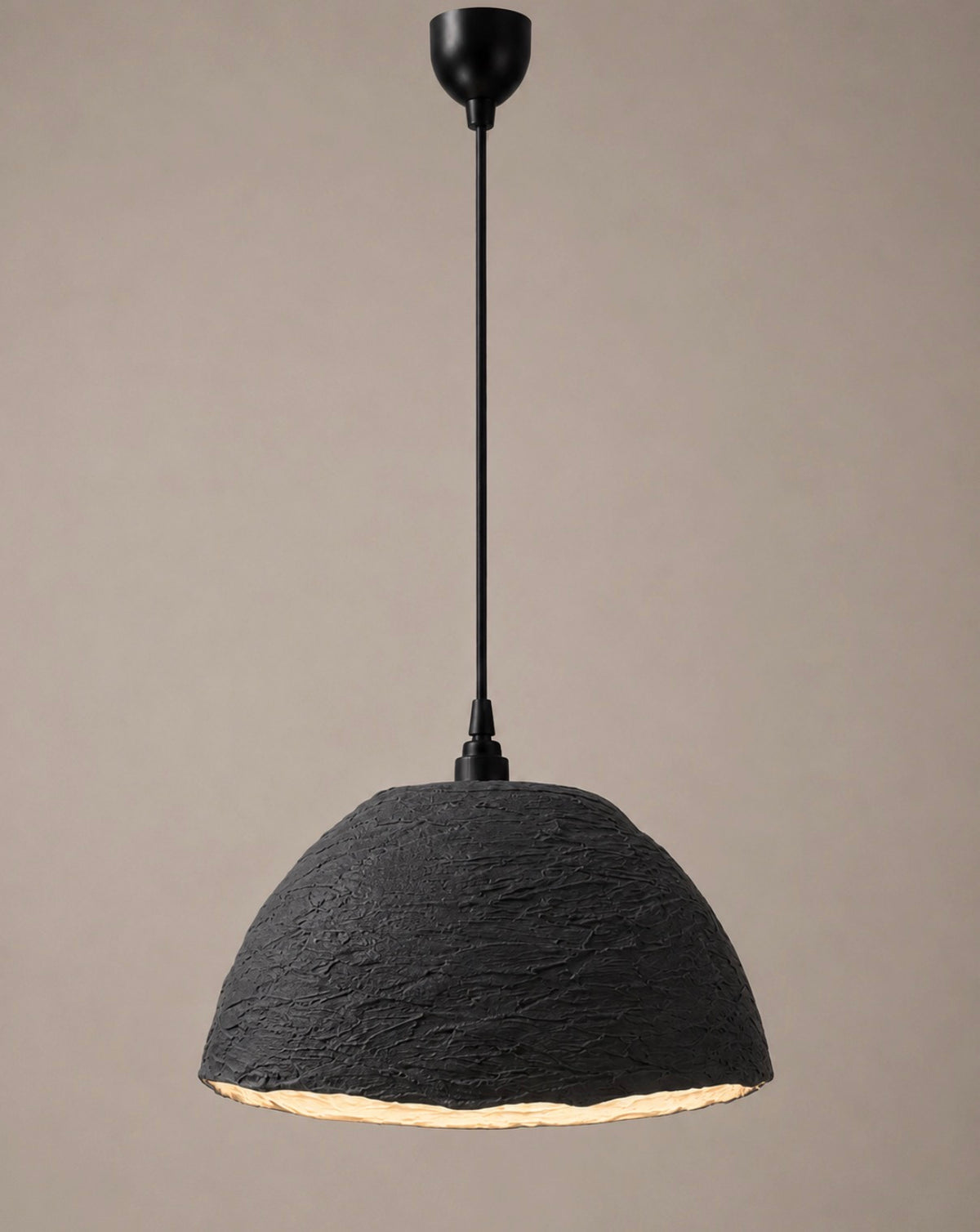 A modern pendant light with a heavily textured charcoal dome shade and matte black rod and canopy, shown against a soft warm grey background.
