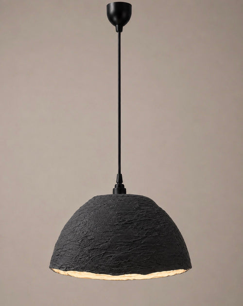 A modern pendant light with a heavily textured charcoal dome shade and matte black rod and canopy, shown against a soft warm grey background.