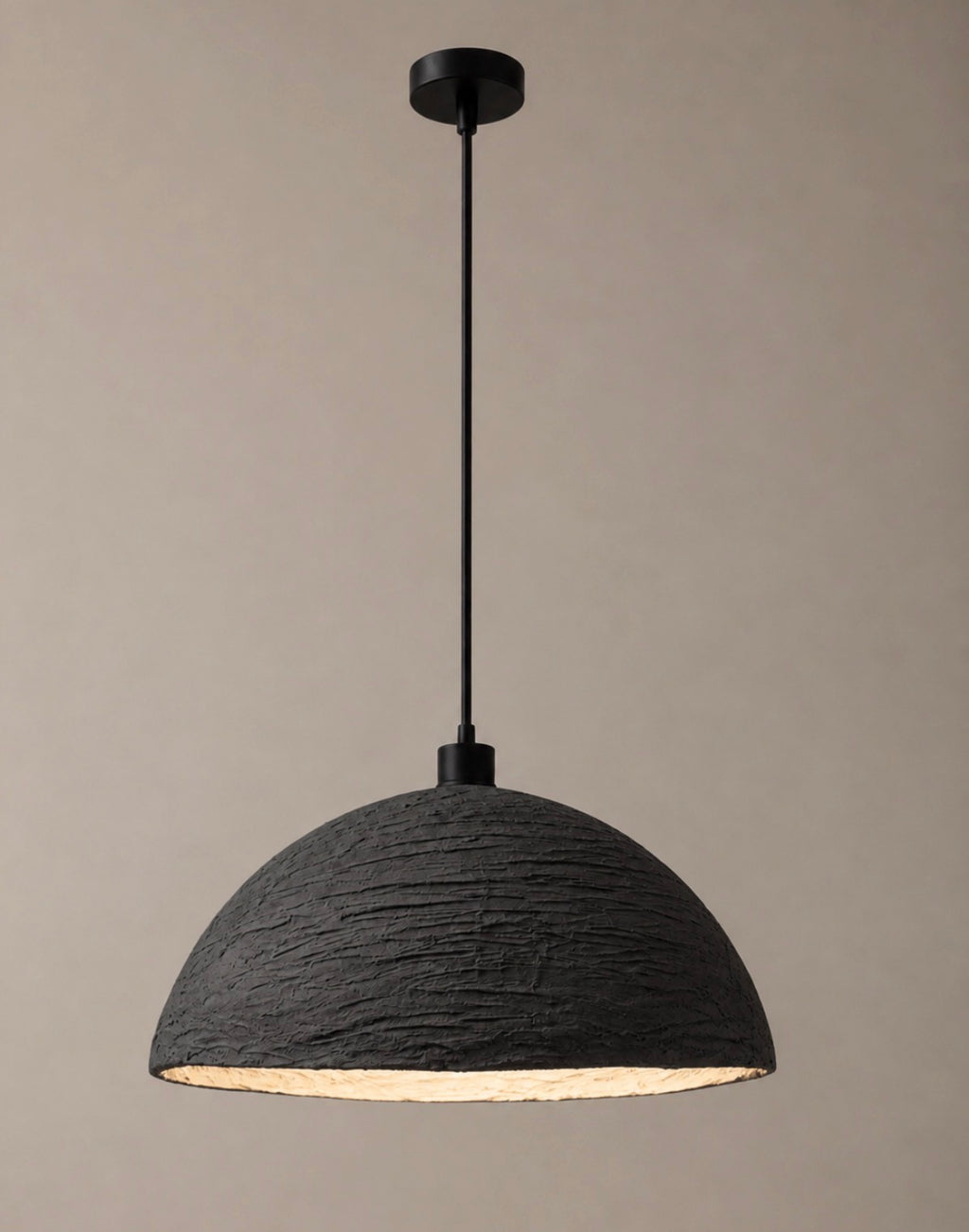 A sculptural pendant light with a wide textured charcoal dome shade and matte black suspension cord, shown against a warm neutral background
