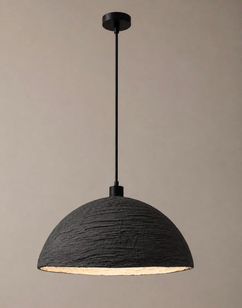 A sculptural pendant light with a wide textured charcoal dome shade and matte black suspension cord, shown against a warm neutral background